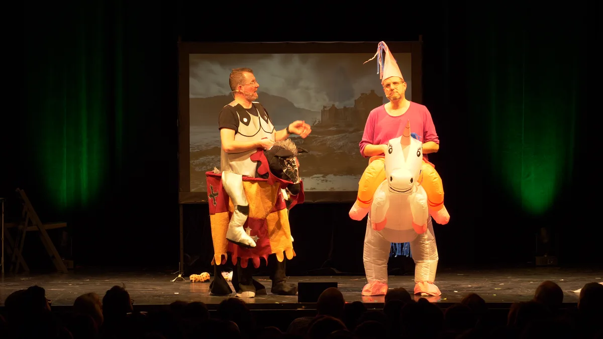 In ihrem ersten Bühnenprogramm galoppierten sie auf einem Steckenpferd und einem Einhorn. Das Comedy-Duo Die Zwillinge auf der Bühne, einer sitzt auf einem Einhorn, der andere auf einem Steckenpferd.